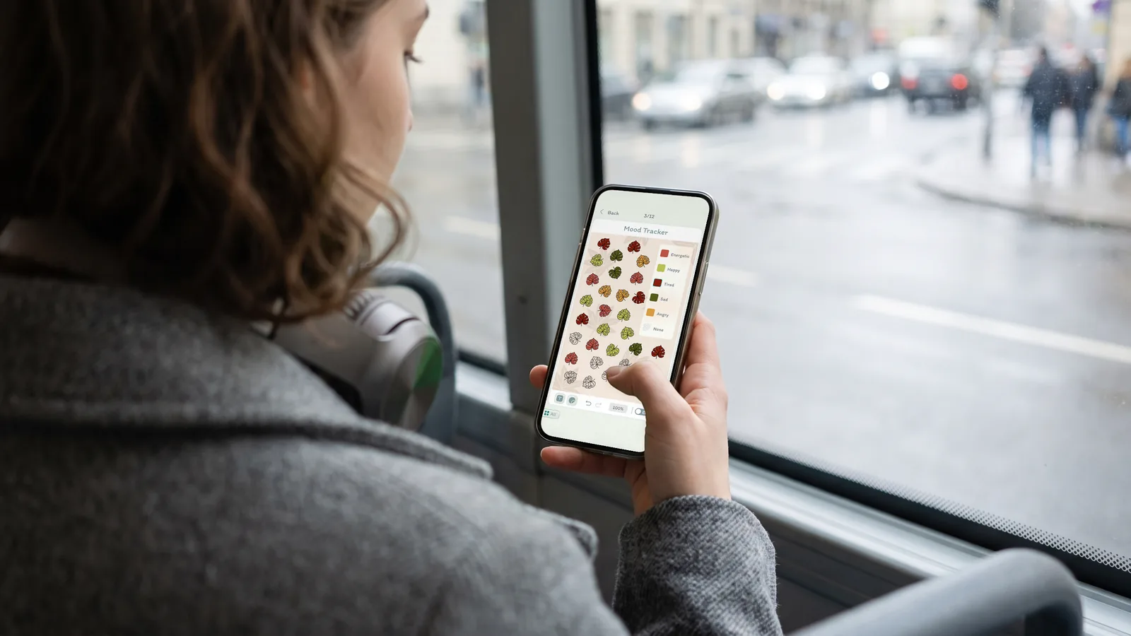 A woman on a city bus, her phone open to a DayBloq Mood Tracker page where each leaf is a day