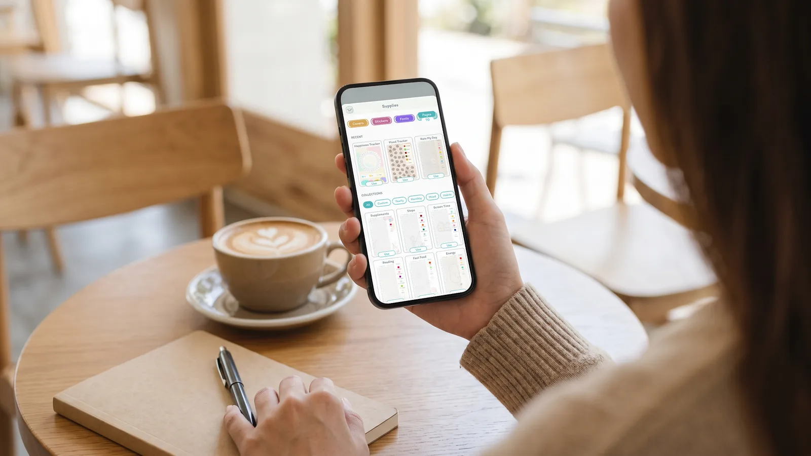 A woman at a cafe table with a latte and a paper notebook, browsing page layouts in DayBloq's Supplies, Pages