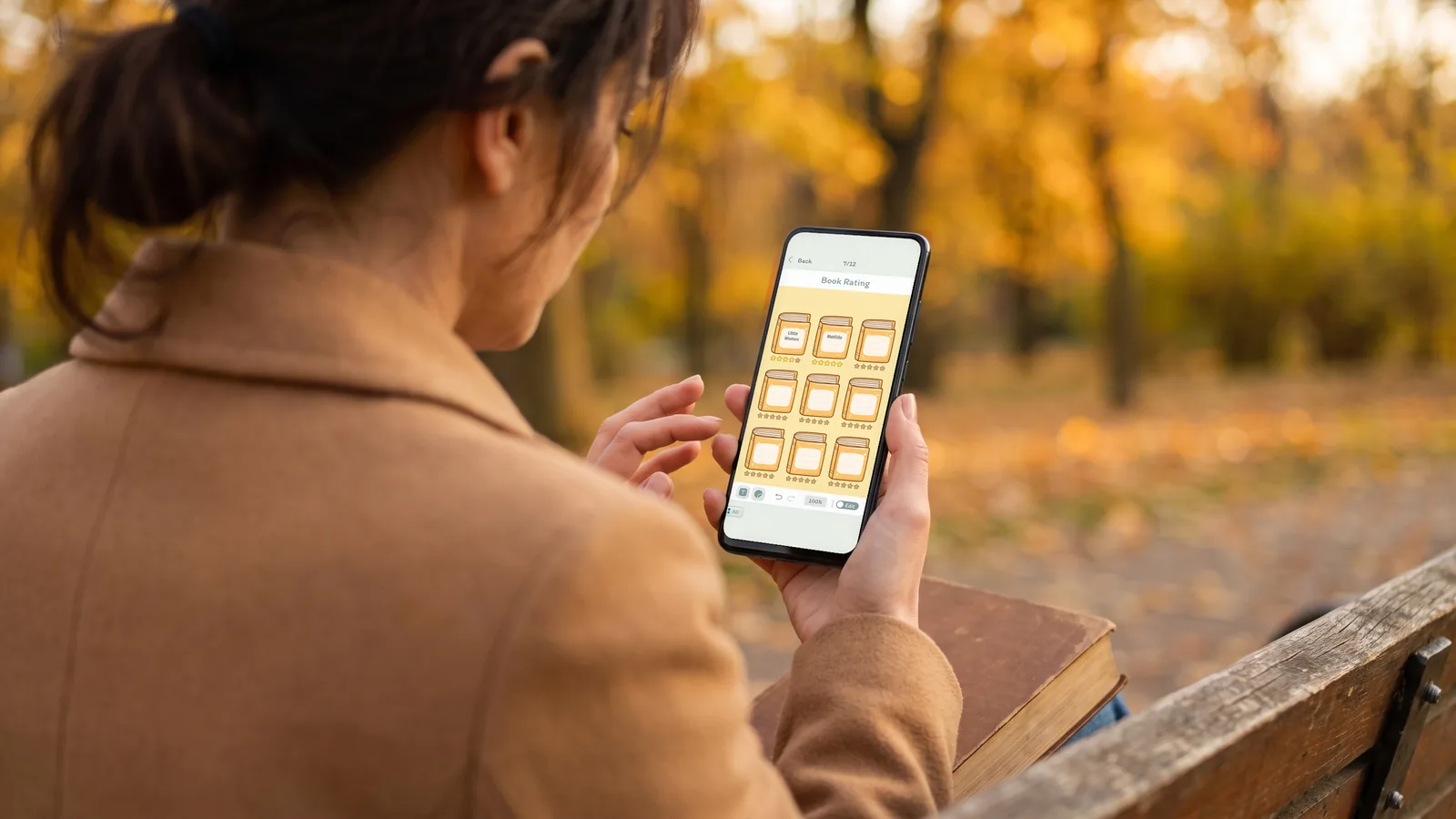 A woman on a park bench in autumn, a book on her lap, rating books on a DayBloq Book Rating page